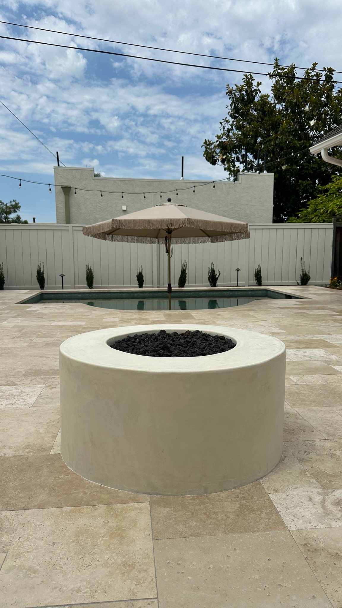 Round concrete fire pit on a travertine pool deck