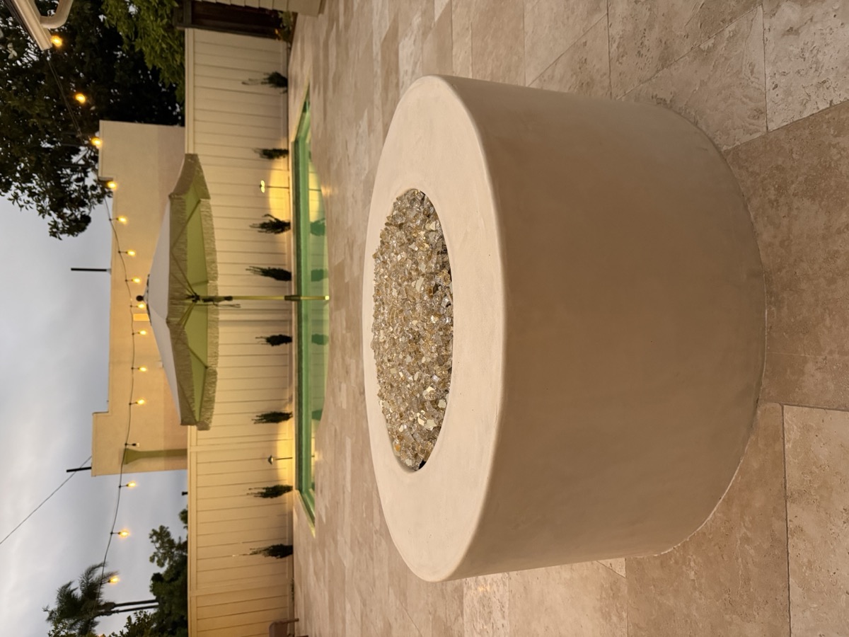 Custom round fire pit on travertine patio with evening string lights