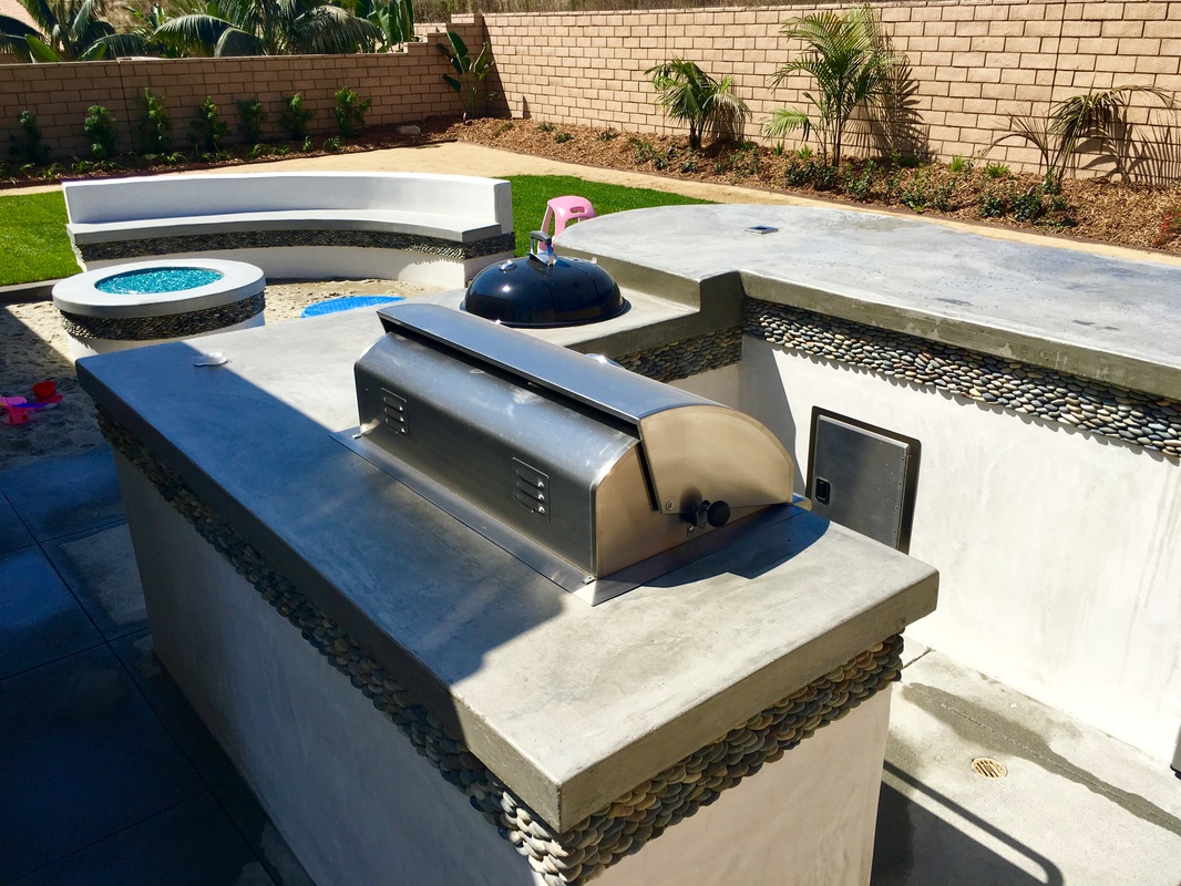 Built-in outdoor kitchen with grill and concrete counters by Arcadian Landscape