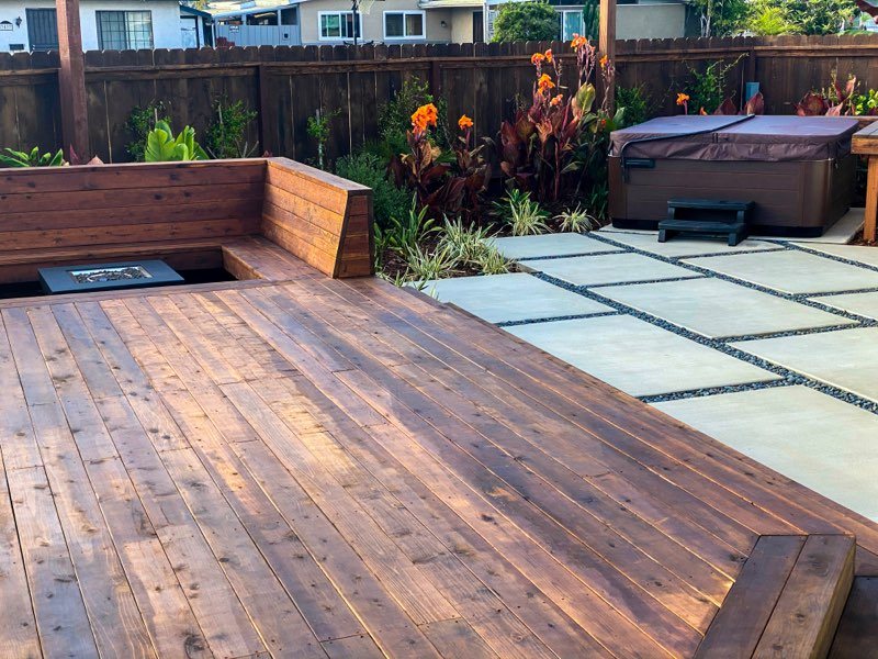 Wood deck with built-in bench next to large concrete pavers and a spa